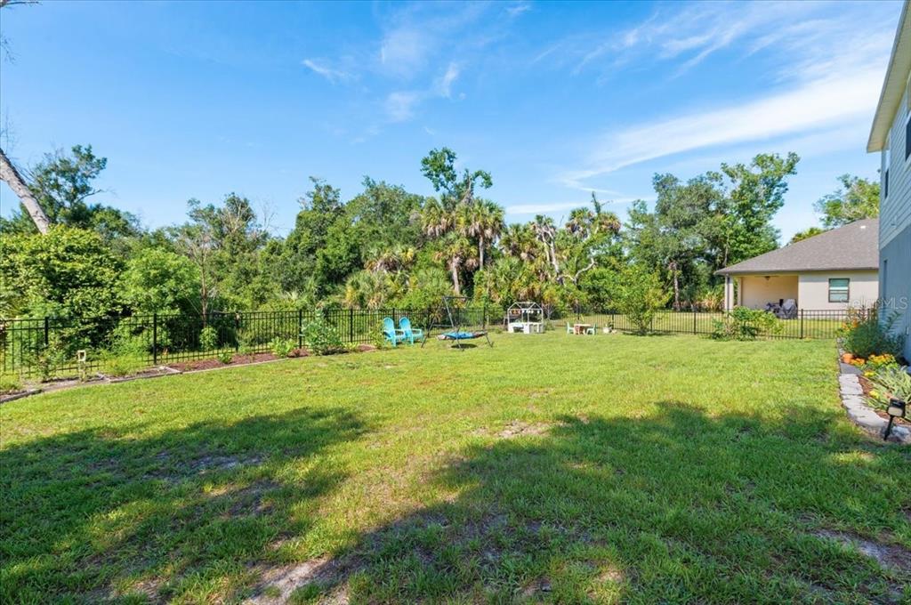 A backyard with a green lawn, a black metal fence, and surrounding trees — 2737 E PRICE BOULEVARD, NORTH PORT, FL