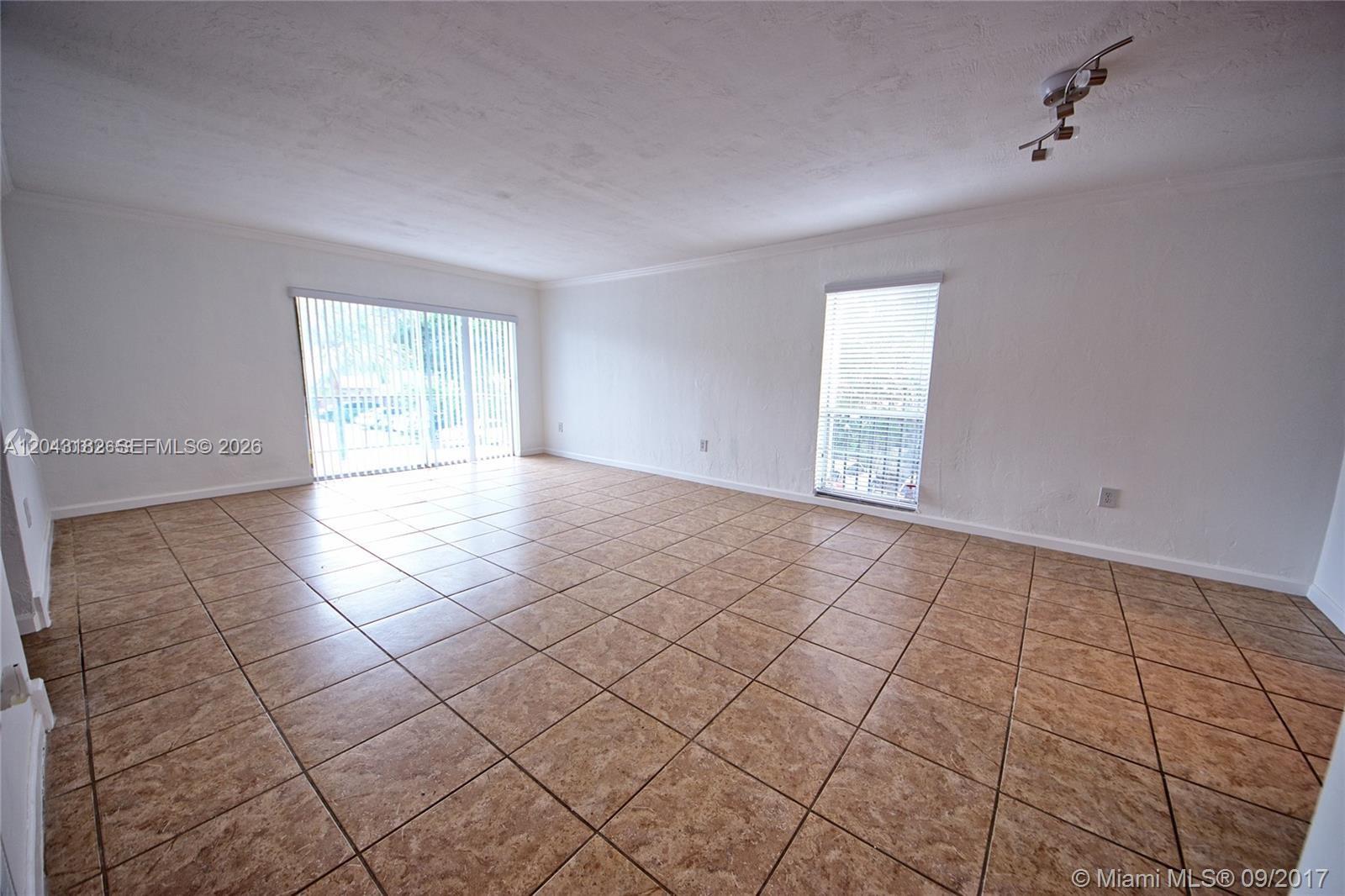 An empty living room features white walls, tan tile flooring, and two windows — 6900 N Kendall Dr # A209, Pinecrest FL 33156, PINECREST, FL