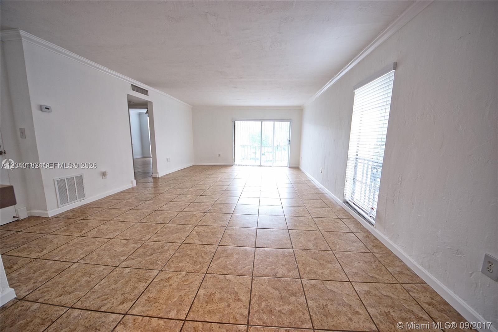 An empty living room features beige tile flooring, white walls, and a sliding glass door — 6900 N Kendall Dr # A209, Pinecrest FL 33156, PINECREST, FL