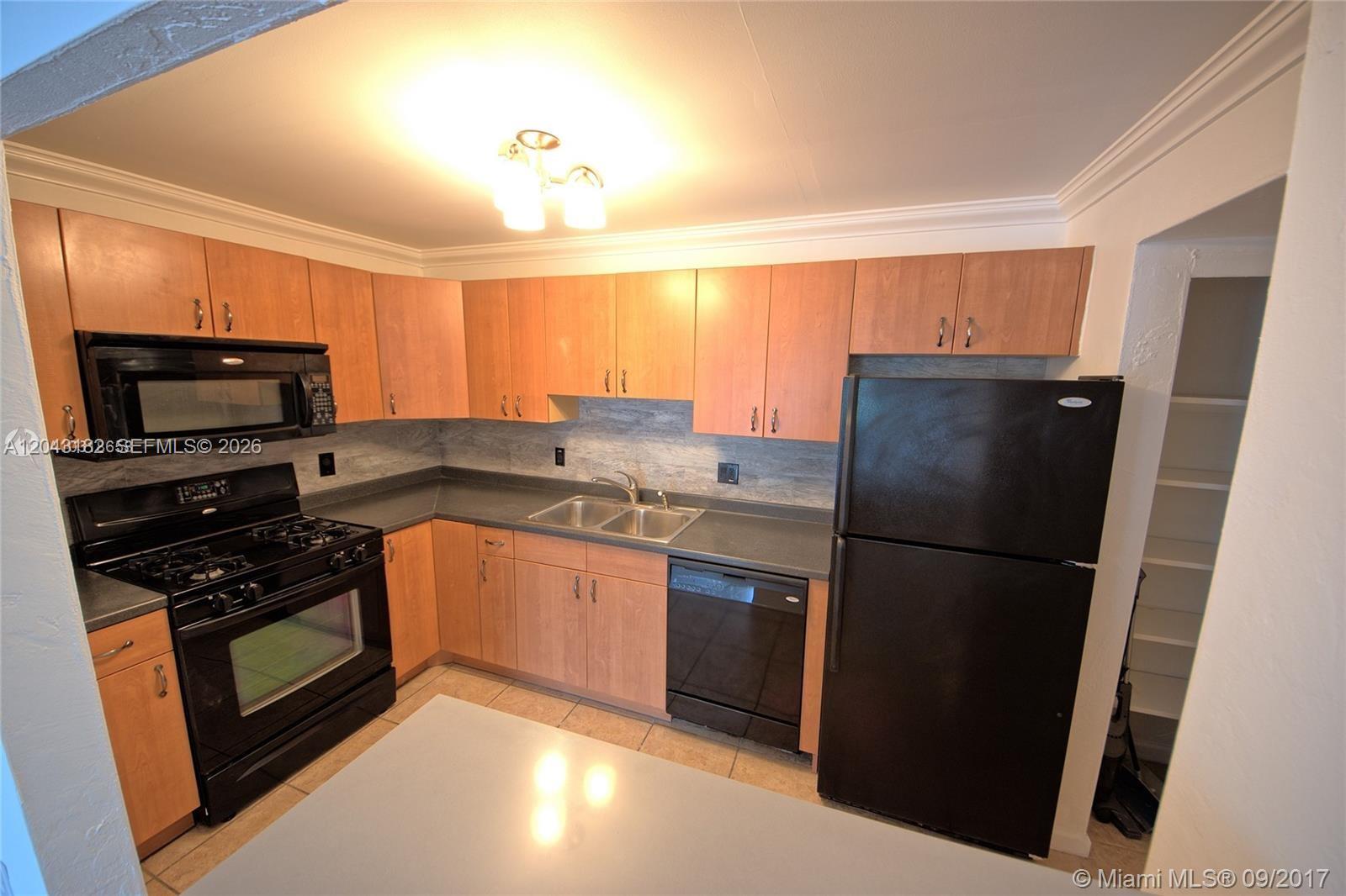 A kitchen features light wood cabinets, black appliances, gray countertops, and a tile floor — 6900 N Kendall Dr # A209, Pinecrest FL 33156, PINECREST, FL