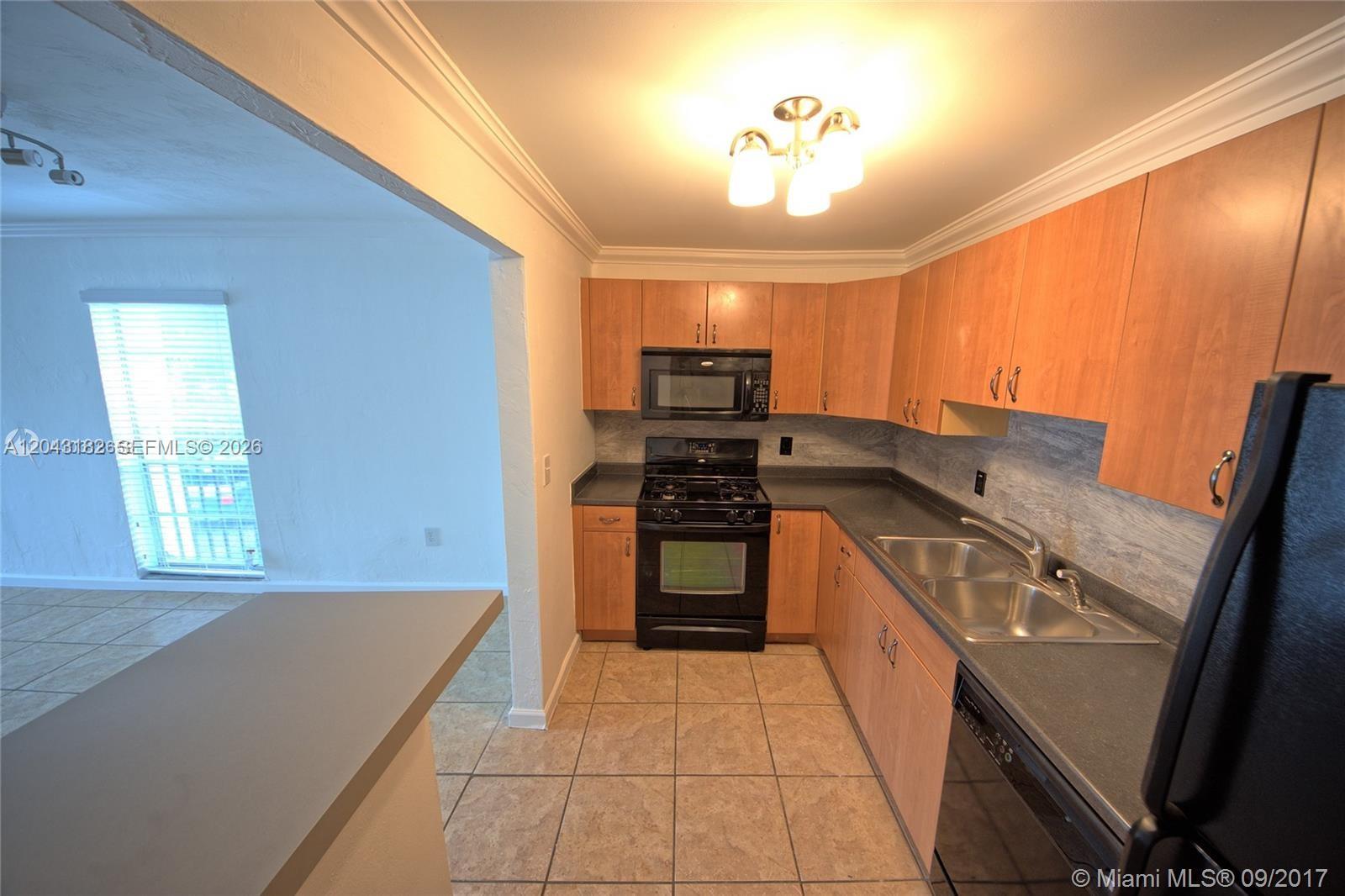 A kitchen features light wood cabinets, black appliances, dark countertops, and tile flooring — 6900 N Kendall Dr # A209, Pinecrest FL 33156, PINECREST, FL