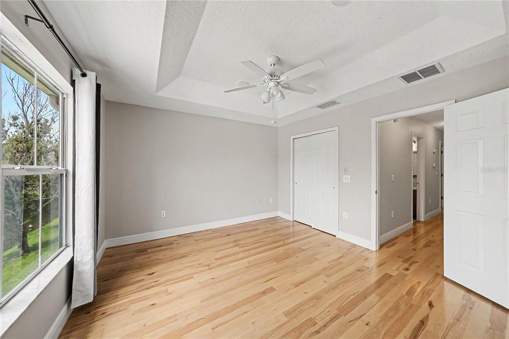 A bedroom with light gray walls, hardwood floors, a tray ceiling, and a ceiling fan — 8106 SILENT CREEK DRIVE, TAMPA, FL