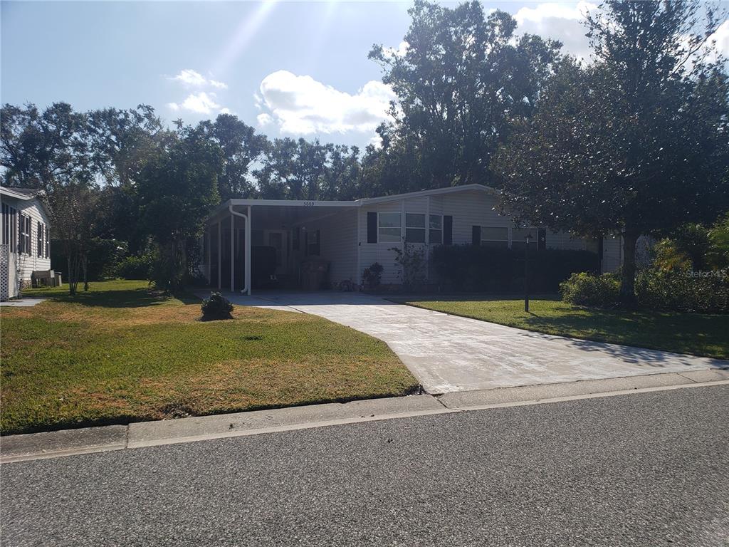A single-story manufactured home features a concrete driveway, a carport, and a grassy front yard — 5009 EL DESTINO DRIVE, LEESBURG, FL