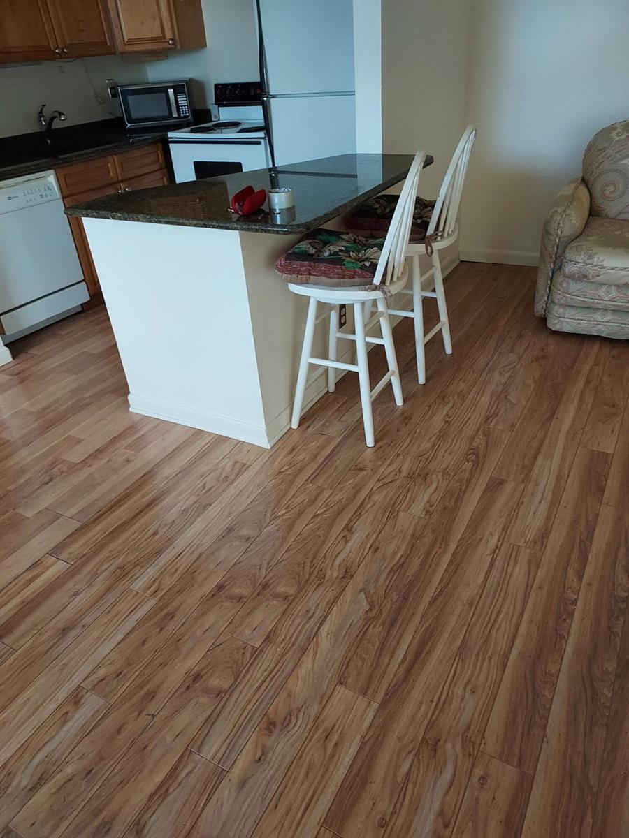 A kitchen island with a dark granite countertop and two white chairs sits on wood flooring — 261 Coventry K, West Palm Beach FL 33417, WEST PALM BEACH, FL