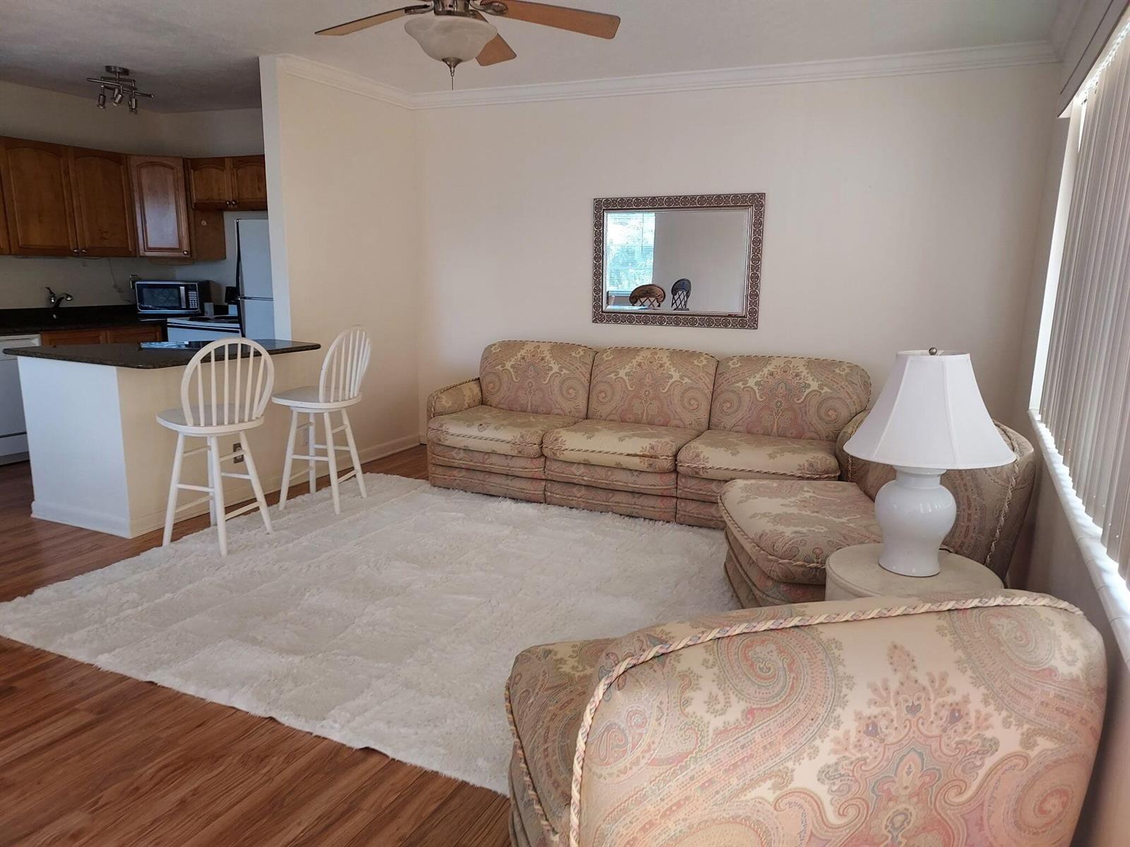A living room with a patterned sectional sofa, white rug, and an adjacent kitchen counter — 261 Coventry K, West Palm Beach FL 33417, WEST PALM BEACH, FL