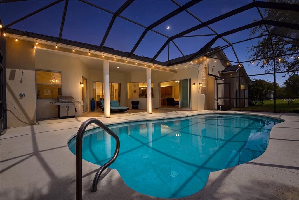A swimming pool sits on a patio enclosed by a screen cage at dusk — 9 LONDON DR, PALM COAST, FL