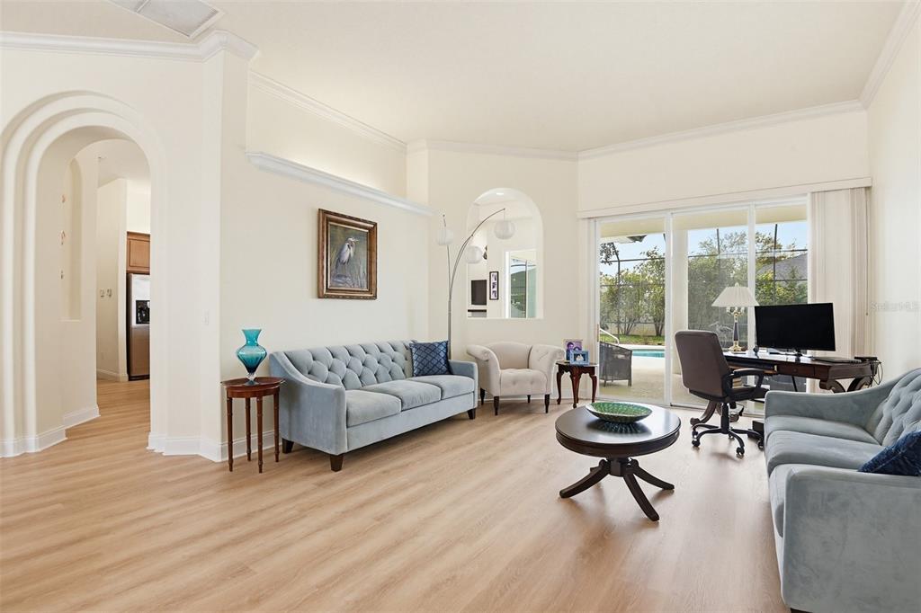 A living room with light wood floors, two blue sofas, a desk, and sliding glass doors — 9 LONDON DR, PALM COAST, FL