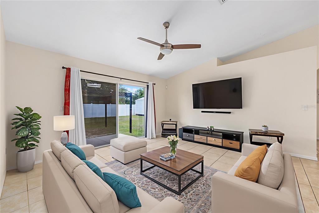 A living room features light-colored sofas, a coffee table, a television, and sliding glass doors — 6568 SW 129TH LANE, OCALA, FL