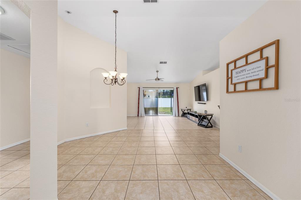 An open-concept living and dining area features tile flooring, a chandelier, and sliding glass doors — 6568 SW 129TH LANE, OCALA, FL
