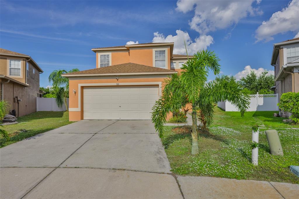 A two-story orange stucco house with a two-car garage and a palm tree in front — 702 CRISTELLE JEAN DRIVE, RUSKIN, FL