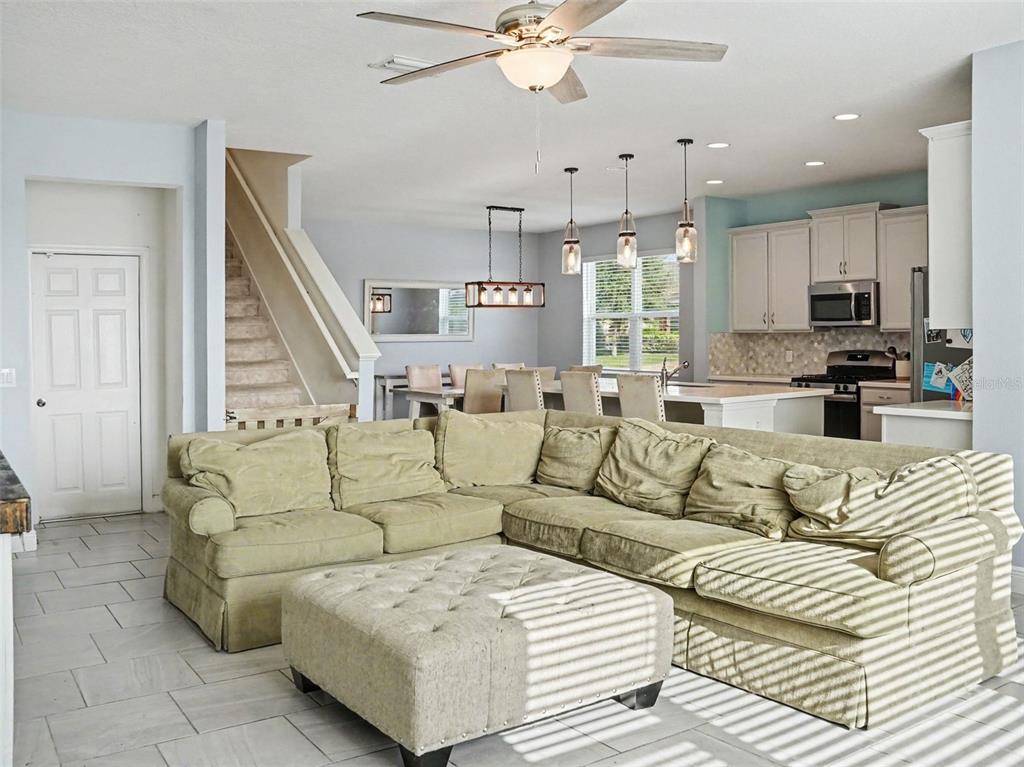 A living room with a large sectional sofa and ottoman opens to a kitchen and dining area — 1401 SHIRA ROAD, MINNEOLA, FL