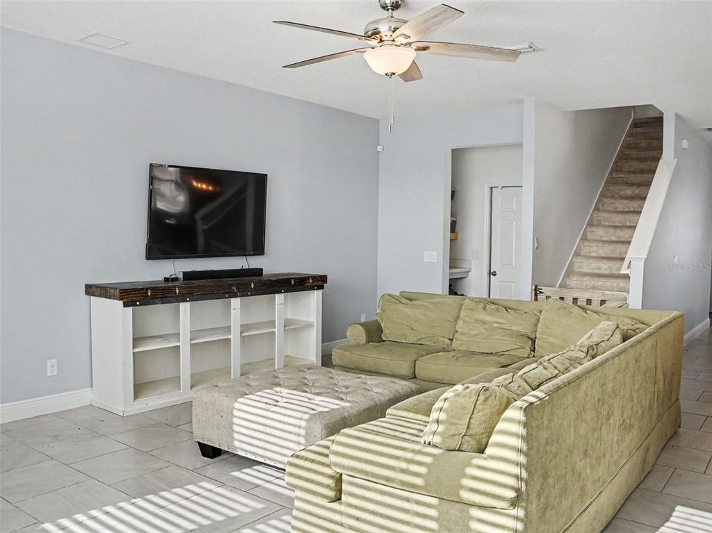 A living room features a sectional sofa, a television, and a staircase in the background — 1401 SHIRA ROAD, MINNEOLA, FL