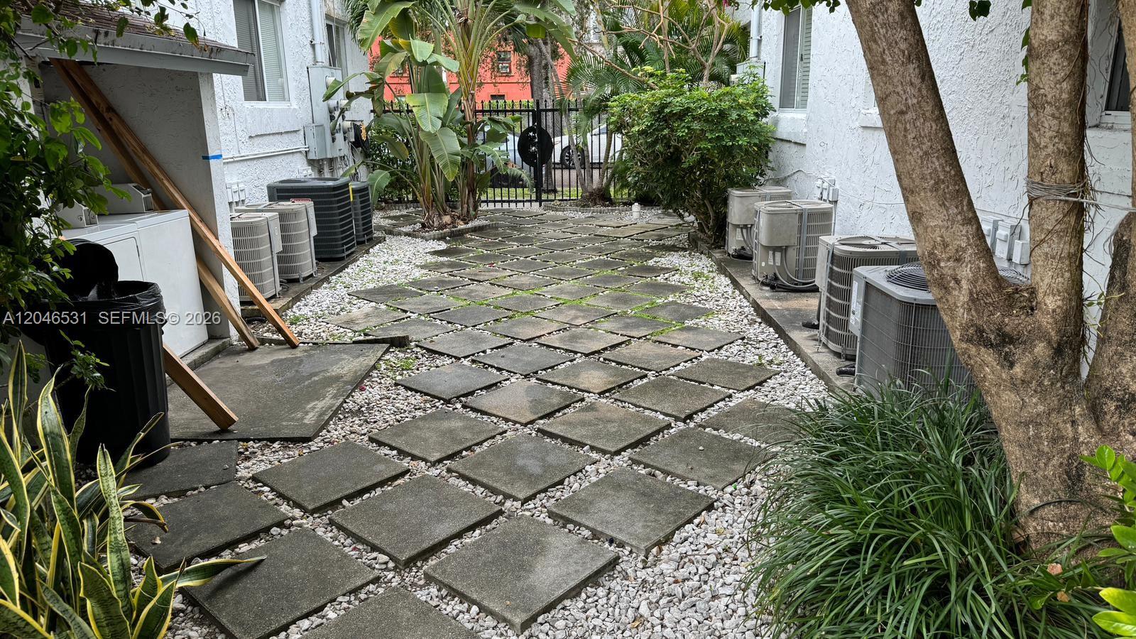 A narrow outdoor courtyard features square concrete pavers surrounded by gravel and multiple air-conditioning units — 103 NW 6th Ave # 2, Miami FL 33128, MIAMI, FL