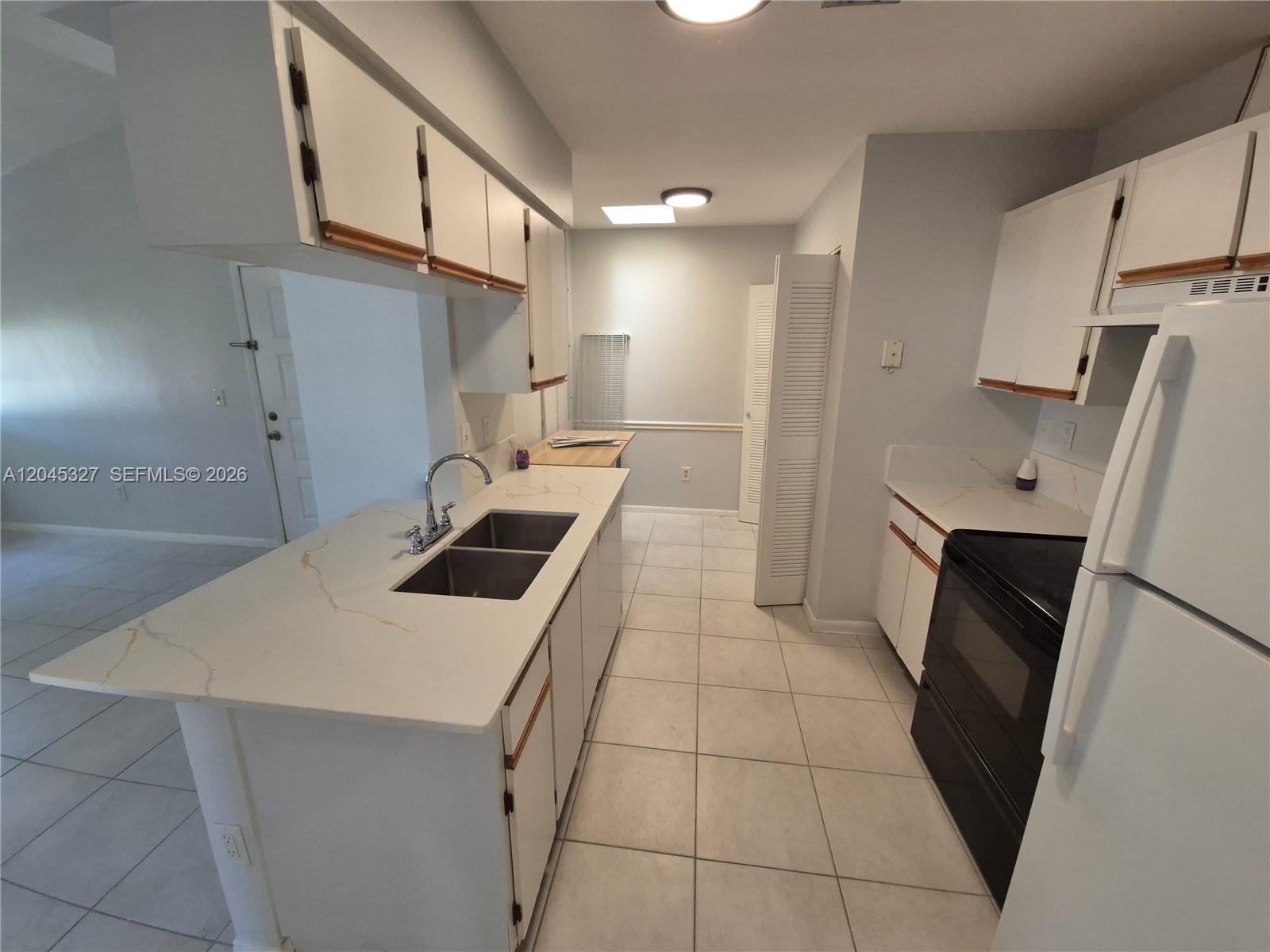 A kitchen features white cabinets, a marble-look countertop, a double sink, and black appliances — 18310 NW 68th Ave # P, Hialeah FL 33015, HIALEAH, FL
