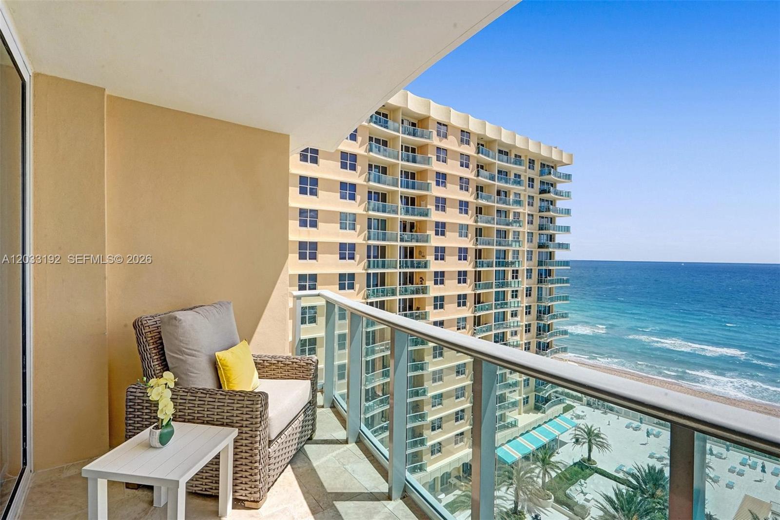 A balcony with a wicker chair overlooks a tall apartment building and the ocean — 2501 S Ocean Dr, Hollywood FL 33019, HOLLYWOOD, FL