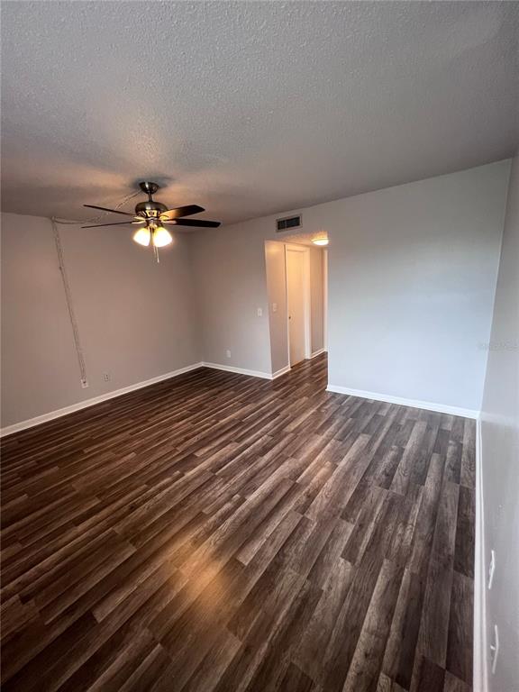 An empty room features wood-look flooring, a ceiling fan, and a doorway leading to a hallway — 6338 NEWTOWN CIRCLE UNIT 38C5, TAMPA, FL