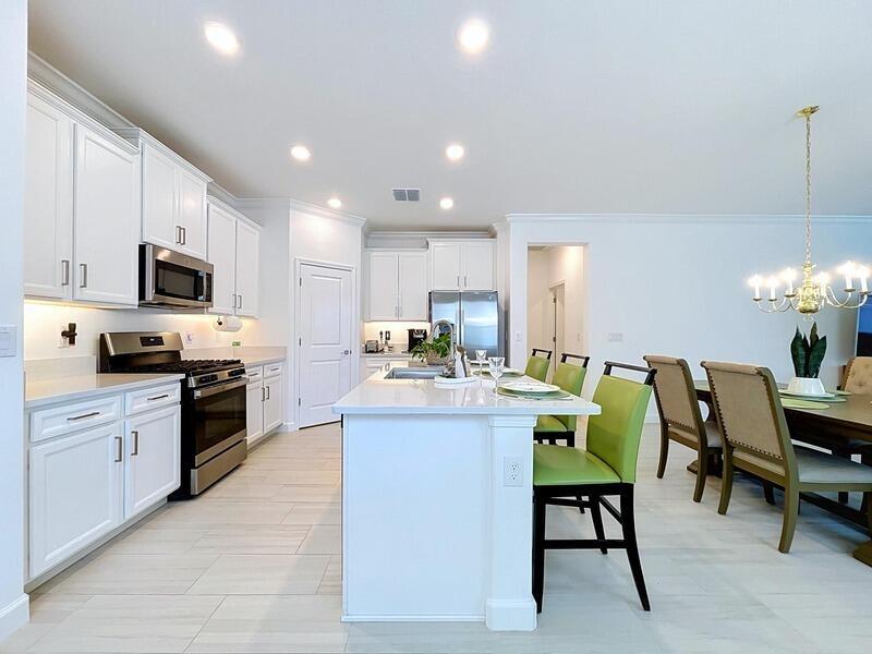 A modern kitchen features white cabinetry, stainless steel appliances, a central island, and dining area — 17228 Star Banks Street, FL 33598, FL