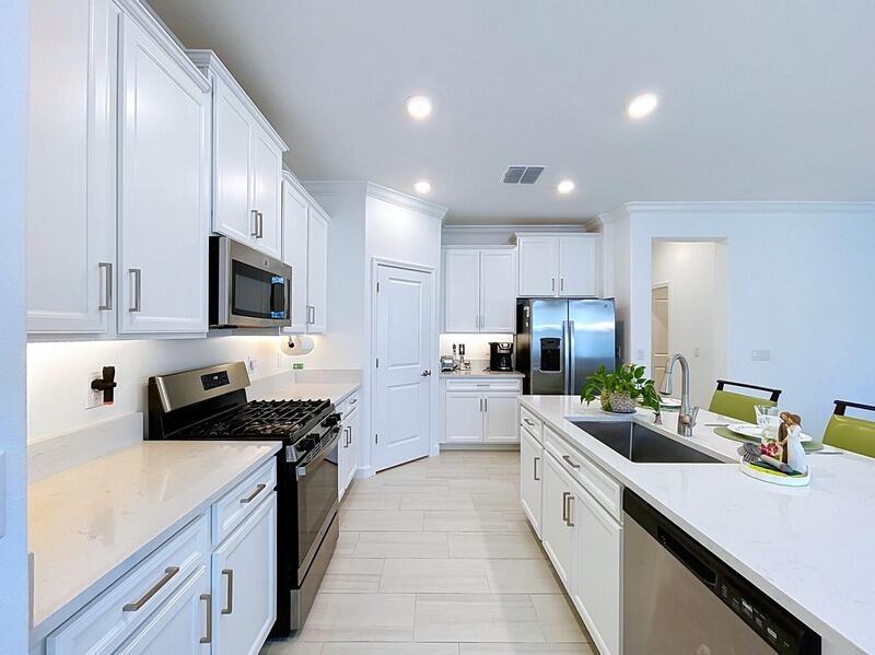 A modern white kitchen features stainless steel appliances, quartz countertops, and light tile flooring — 17228 Star Banks Street, FL 33598, FL