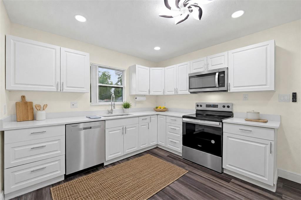 A kitchen with white cabinets, stainless steel appliances, white countertops, and dark wood-look flooring — 9402 N 12TH ST, TAMPA, FL