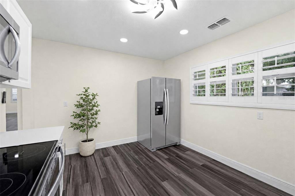 A kitchen with dark wood-look flooring, white walls, a stainless steel refrigerator, and plantation shutters — 9402 N 12TH ST, TAMPA, FL