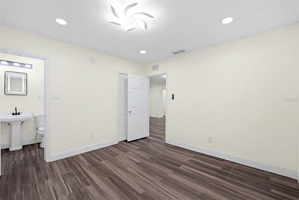 A bedroom with light walls, wood-look flooring, a ceiling light fixture, and an attached bathroom — 9402 N 12TH ST, TAMPA, FL