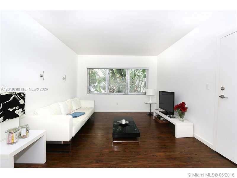 A living room features white walls, dark wood flooring, a white sofa, and a television — 1616 Euclid Ave # 6, Miami Beach FL 33139, MIAMI BEACH, FL