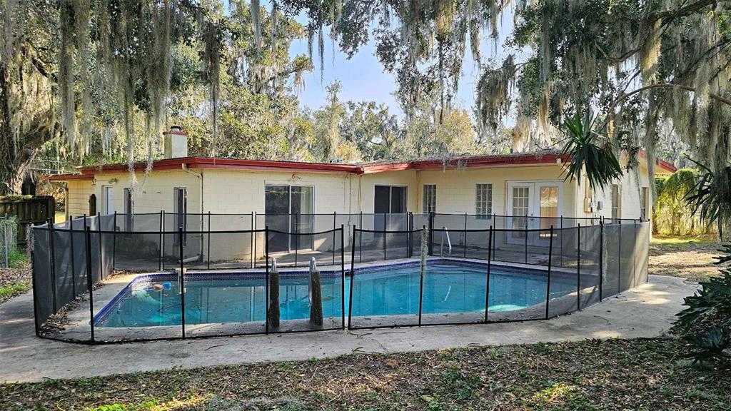 A single-story house with a swimming pool enclosed by a black mesh safety fence — 1017 CYPRESS STREET, LEESBURG, FL