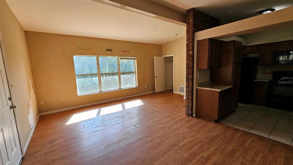 An open-concept living room with wood-look flooring connects to a kitchen with dark cabinets — 1017 CYPRESS STREET, LEESBURG, FL