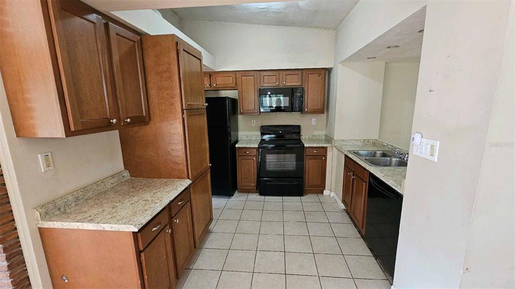 A kitchen with wood cabinets, black appliances, and light-colored countertops over tiled flooring — 1017 CYPRESS STREET, LEESBURG, FL