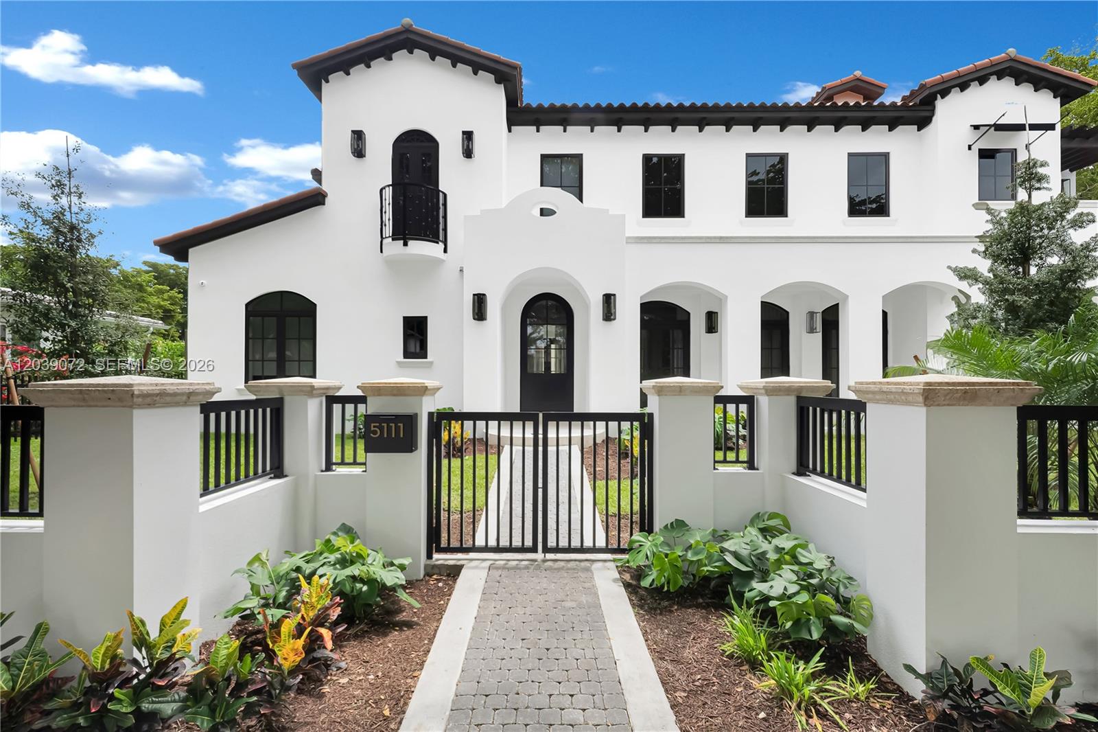 A white two-story Mediterranean-style house features a gated walkway, black trim, and arched entryways — 5111 Alhambra Cir, Coral Gables FL 33146, CORAL GABLES, FL