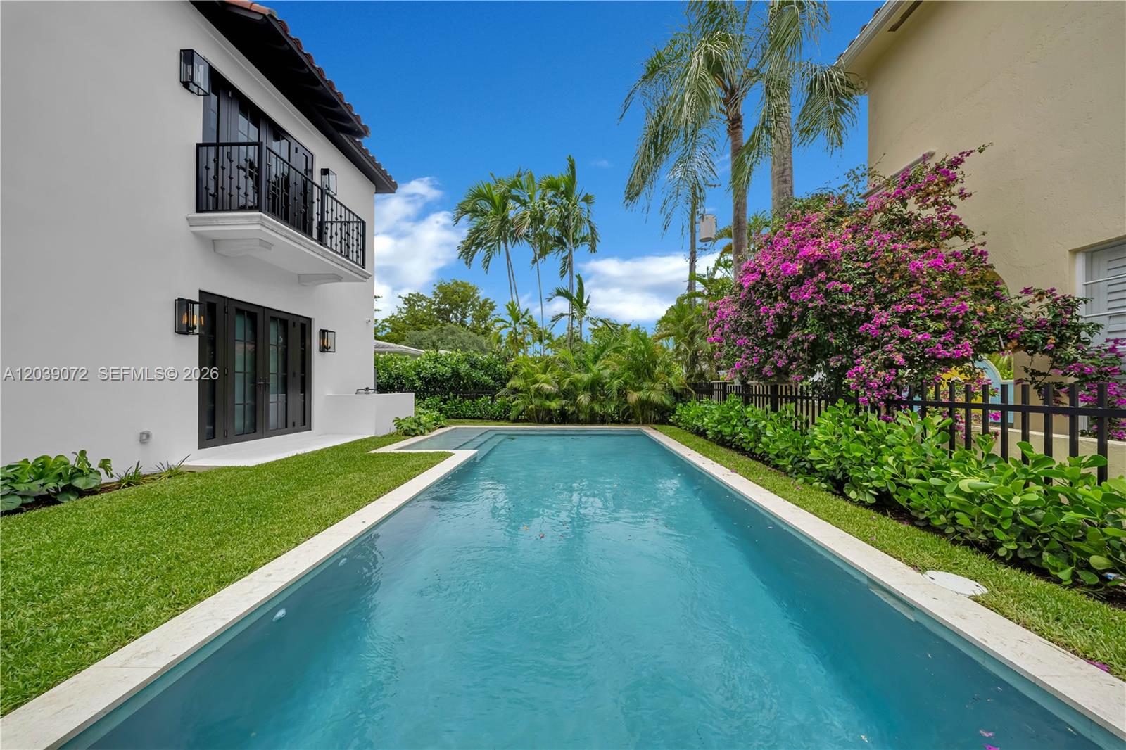 A rectangular swimming pool sits beside a white two-story house with a black balcony — 5111 Alhambra Cir, Coral Gables FL 33146, CORAL GABLES, FL