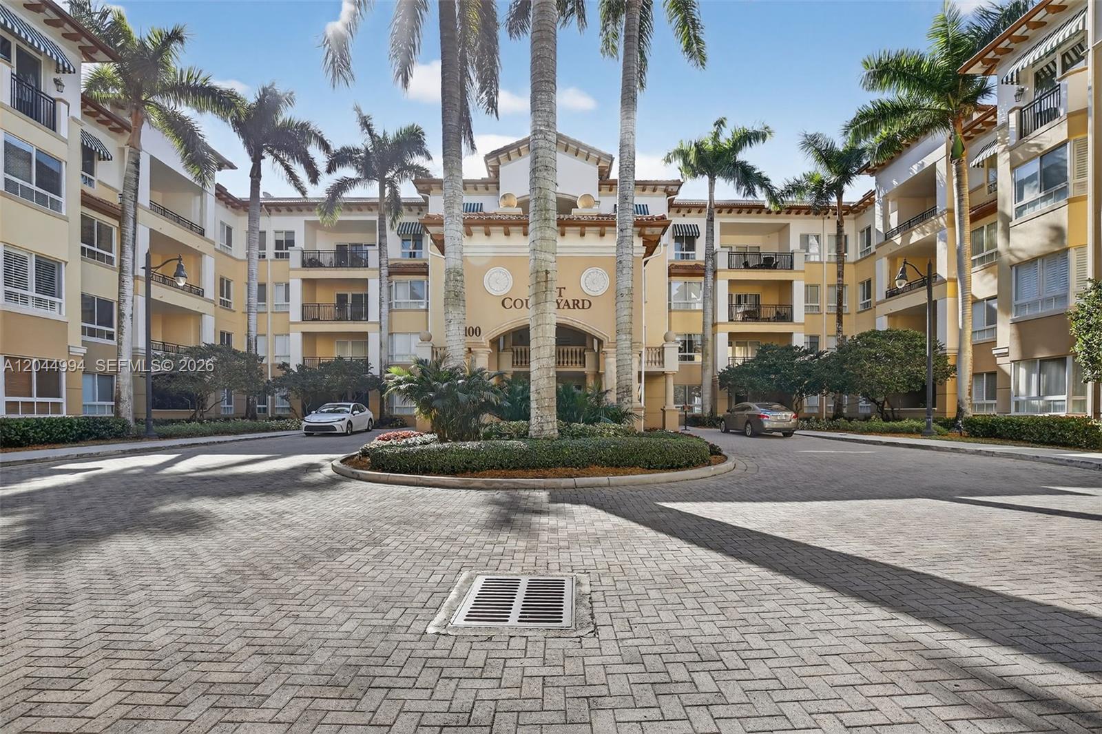 A paved driveway leads to the entrance of a multi-story apartment building with palm trees — WESTON, FL
