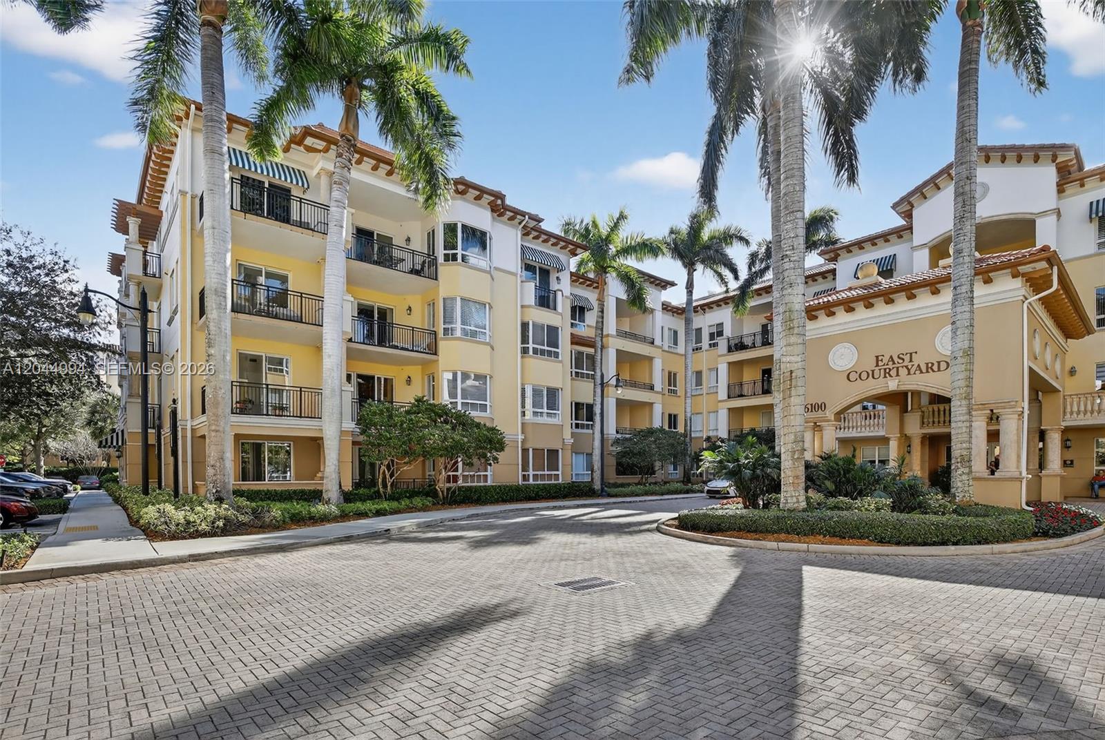 The exterior of a multi-story apartment building features a paved courtyard and palm trees — WESTON, FL