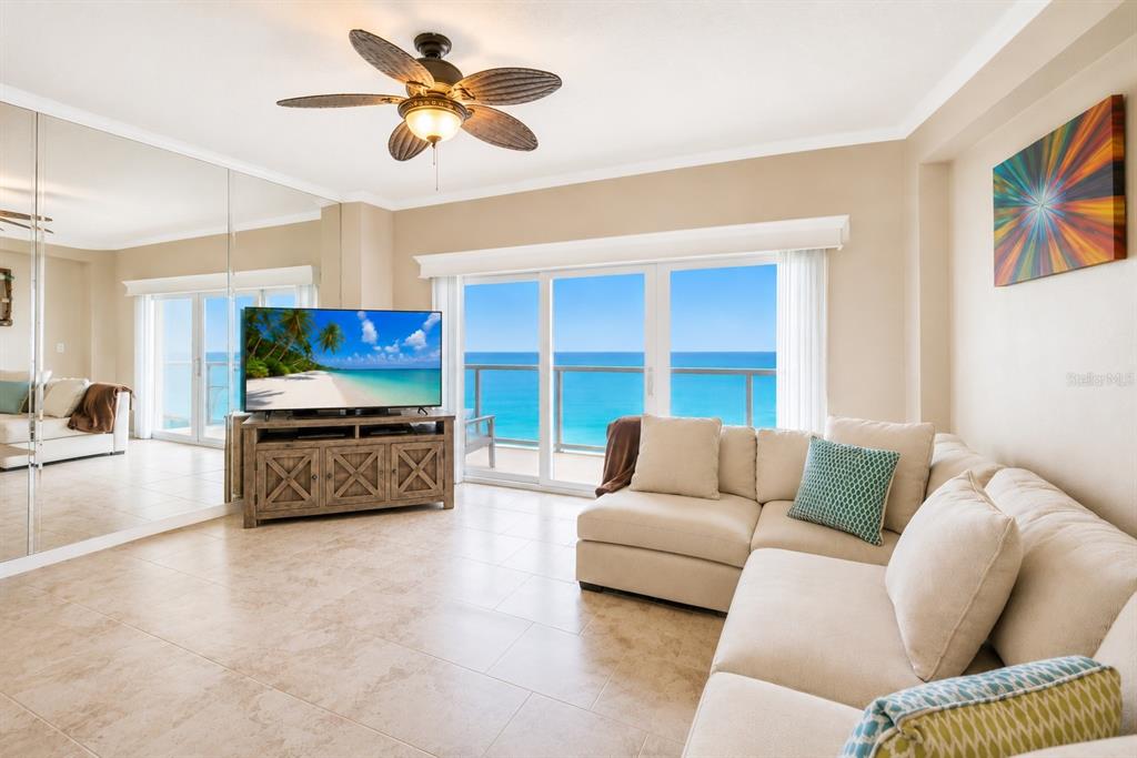 A living room features a beige sectional sofa, a television on a wooden stand, and ocean views — 880 MANDALAY AVENUE UNIT C801, CLEARWATER BEACH, FL