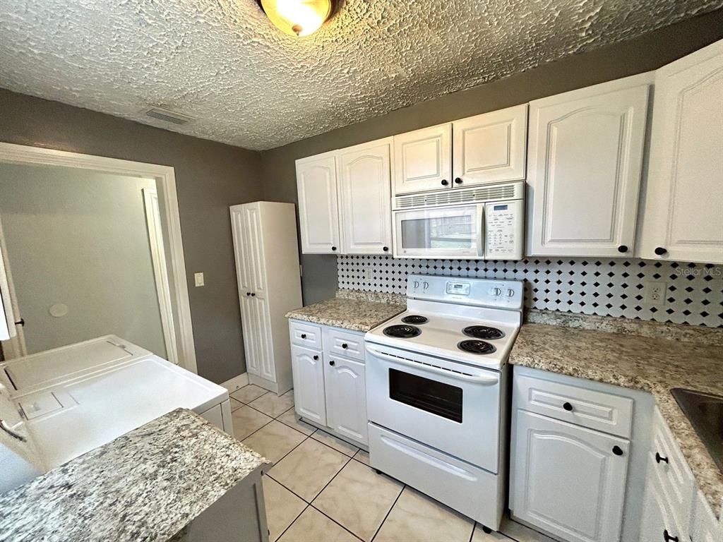 A kitchen features white cabinets, granite countertops, a tiled backsplash, and a white stove — 2308 E 15TH AVENUE, TAMPA, FL
