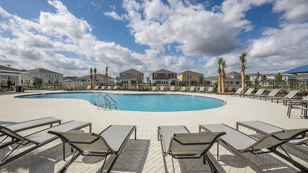 A swimming pool surrounded by lounge chairs and houses under a cloudy blue sky — 511 MOONSTONE COURT, GROVELAND, FL