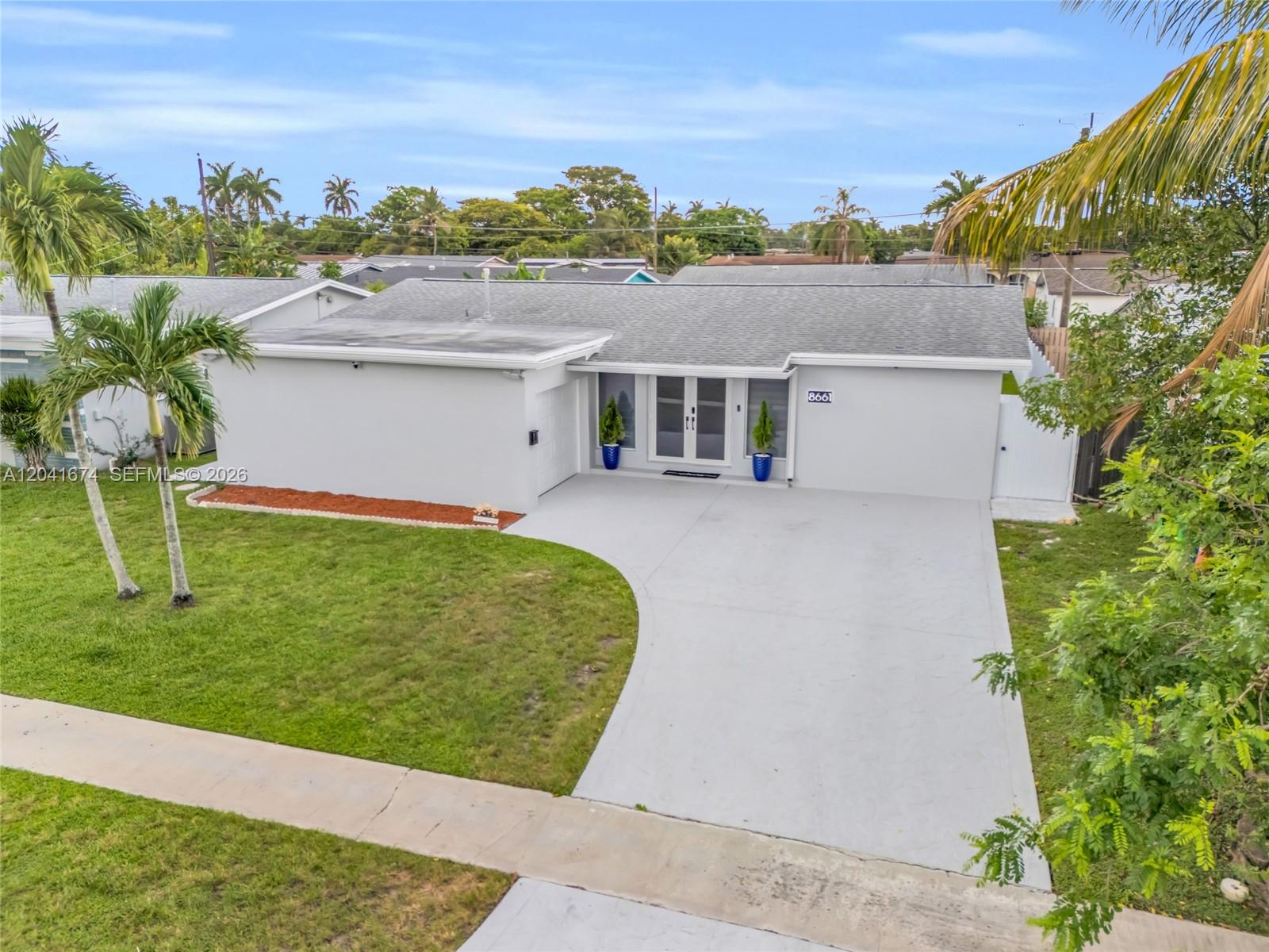 An exterior view of a single-story gray house with a concrete driveway and palm trees — 8661 NW 20th Ct, Sunrise FL 33322, SUNRISE, FL