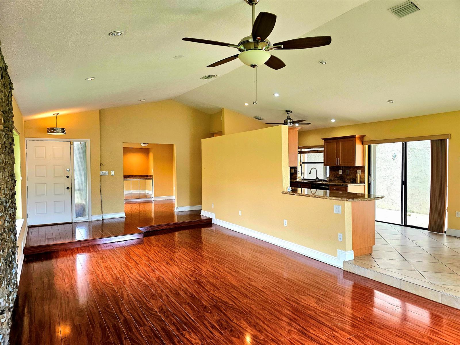 An open-concept living area features hardwood floors, yellow walls, a kitchen island, and vaulted ceilings — 566 Village Lake Drive, Weston FL 33326, WESTON, FL