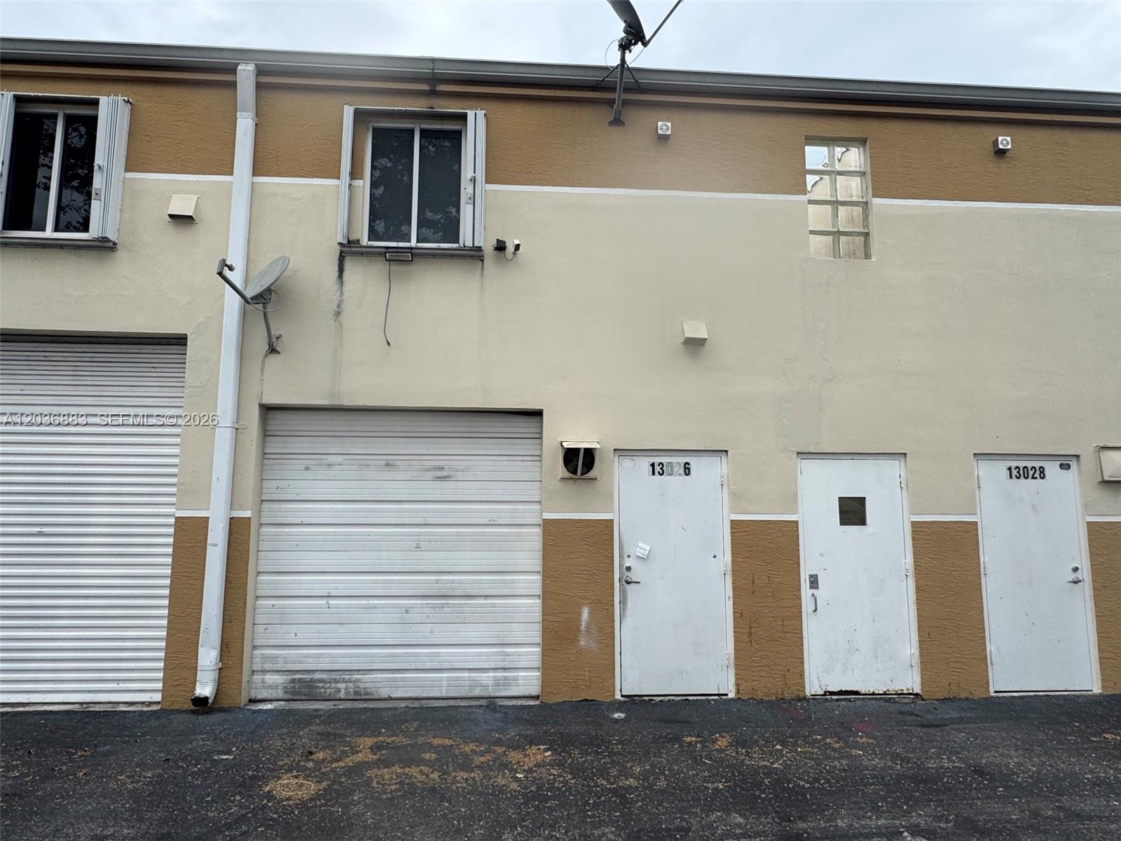 The exterior of a commercial building features a roll-up door and three separate entrance doors — 13026 SW 128th St # 9, Miami FL 33186, MIAMI, FL