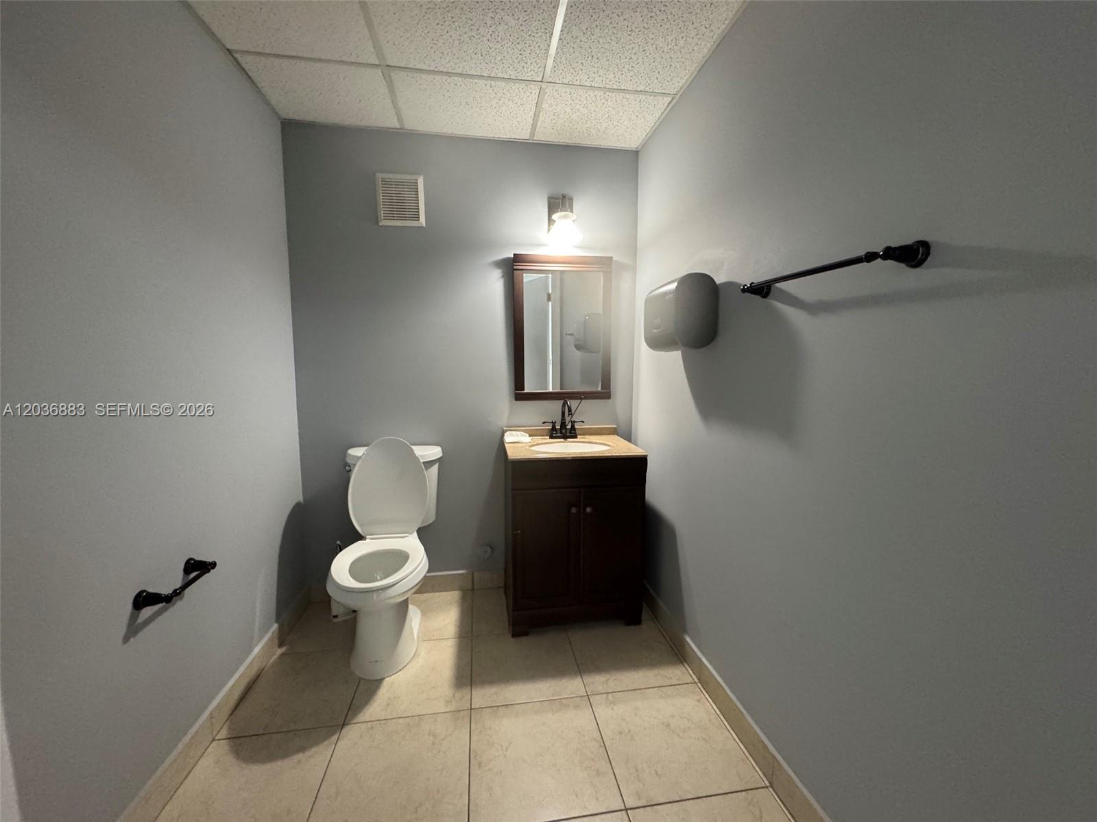 A small bathroom features a toilet, a dark wood vanity, and light-colored floor tiles — 13026 SW 128th St # 9, Miami FL 33186, MIAMI, FL