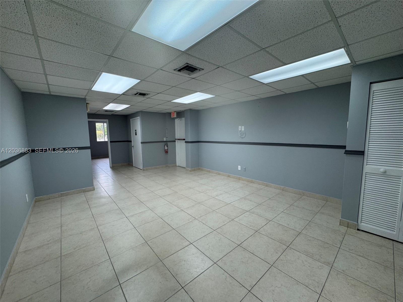 An empty office space features light blue walls, tile flooring, and a drop ceiling — 13026 SW 128th St # 9, Miami FL 33186, MIAMI, FL