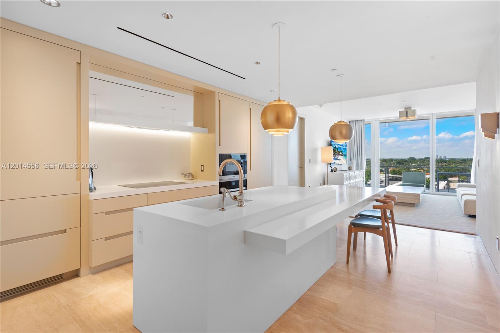 A modern kitchen features light wood cabinetry, a white stone island, and floor-to-ceiling windows — 9111 Collins Ave # 712, Surfside FL 33154, SURFSIDE, FL
