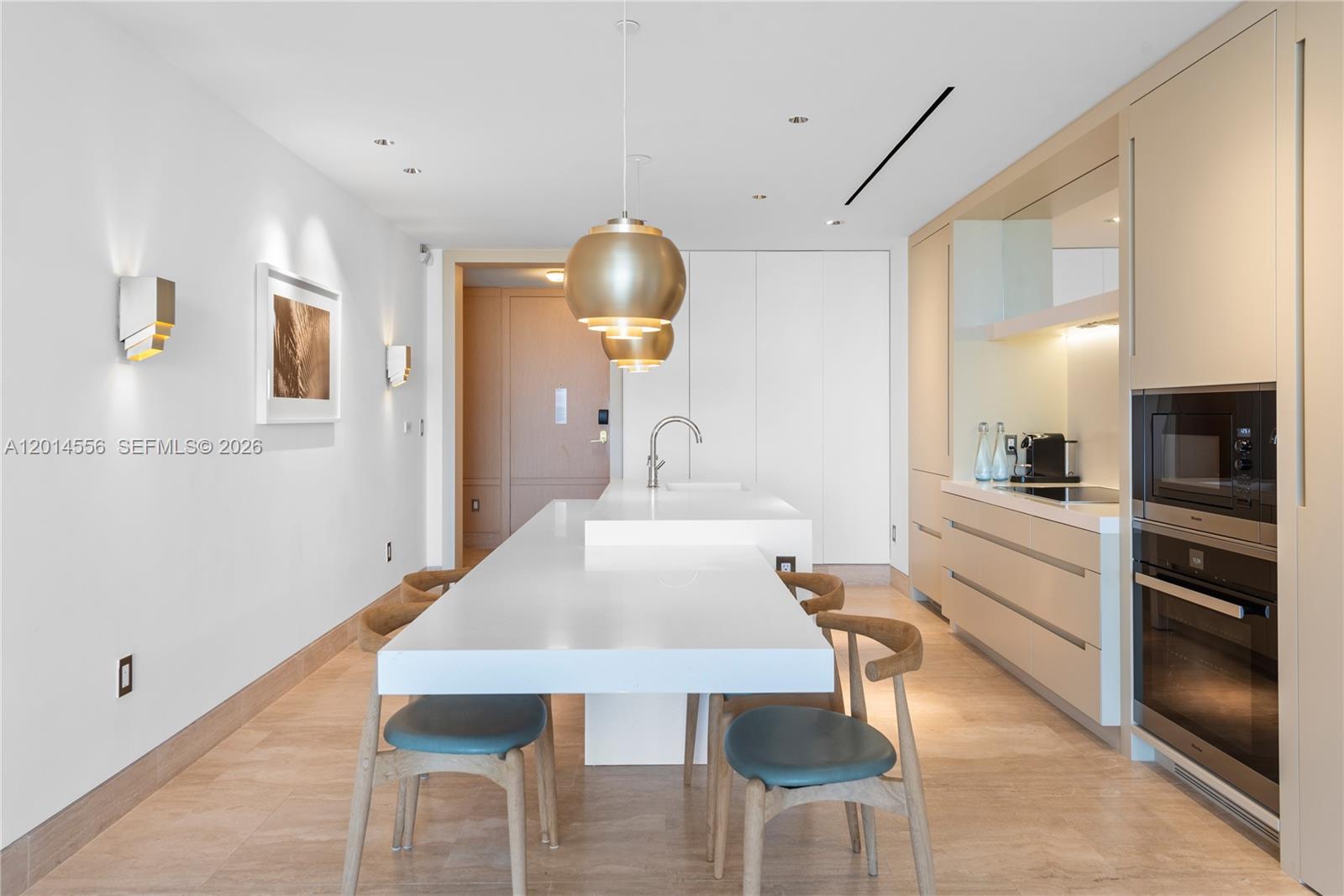 A modern kitchen features a white island with integrated seating and light wood cabinetry — 9111 Collins Ave # 712, Surfside FL 33154, SURFSIDE, FL