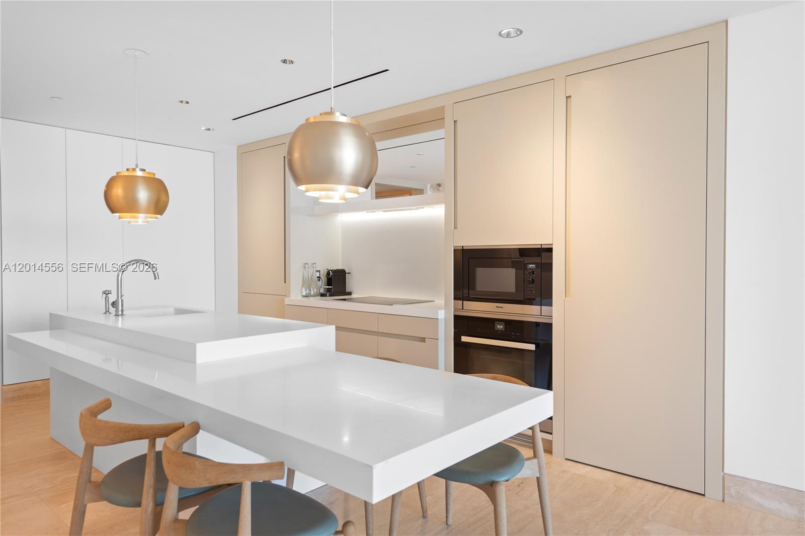 A modern kitchen features a white island, light wood cabinetry, and two gold pendant lights — 9111 Collins Ave # 712, Surfside FL 33154, SURFSIDE, FL