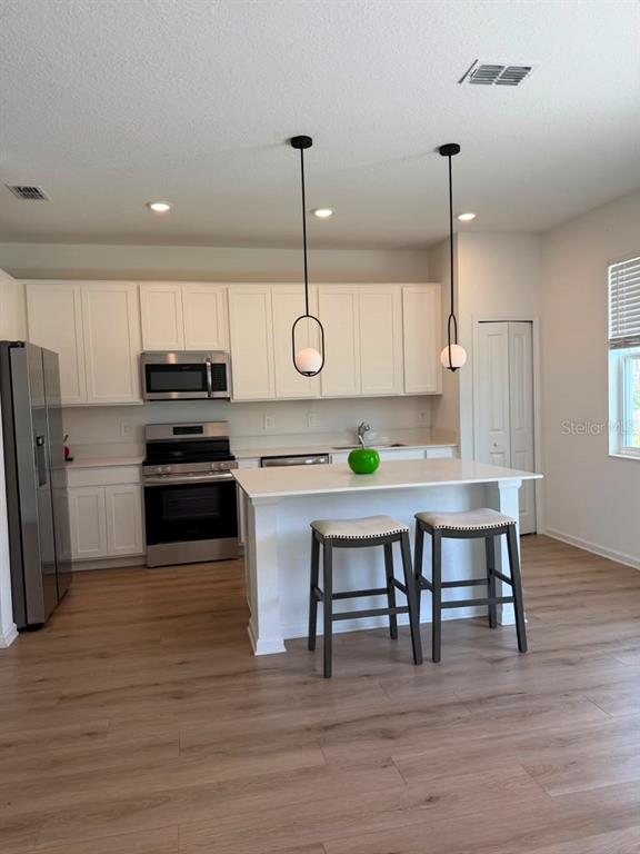 A kitchen features white cabinets, stainless steel appliances, a center island, and two pendant lights — 2954 SAVOIR AVENUE, DAVENPORT, FL