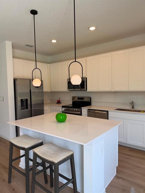 A kitchen features white cabinets, stainless steel appliances, a quartz island, and two pendant lights — 2954 SAVOIR AVENUE, DAVENPORT, FL