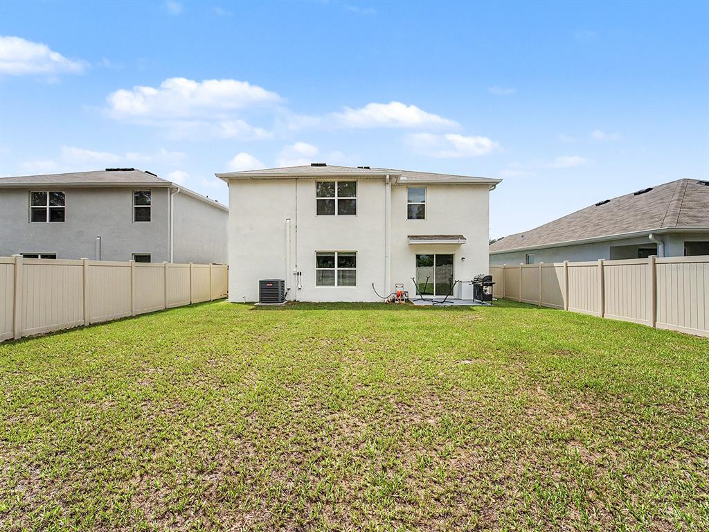 The backyard of a two-story house features a grassy lawn and a vinyl privacy fence — 13484 MYLION WAY, SPRING HILL, FL