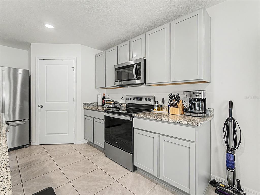 A kitchen features light gray cabinets, granite countertops, stainless steel appliances, and tile flooring — 13484 MYLION WAY, SPRING HILL, FL