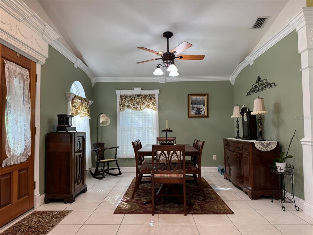 A dining room features sage green walls, tile flooring, a wooden table set, and crown molding — 9814 OSLIN STREET, TAMPA, FL