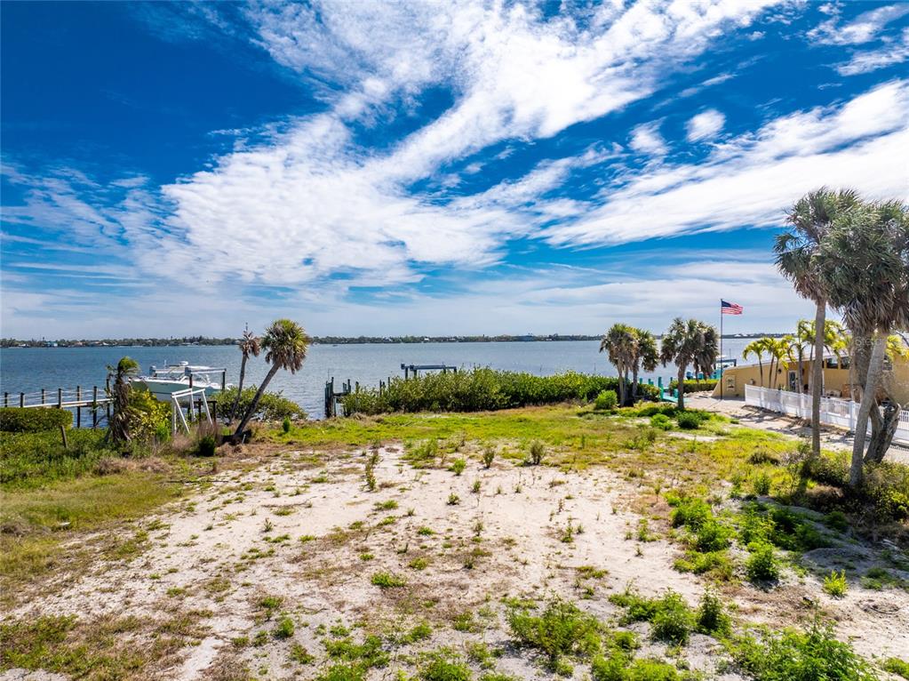 A sandy, grassy waterfront lot features palm trees, a boat dock, and a distant view — 6039 MANASOTA KEY ROAD, ENGLEWOOD, FL
